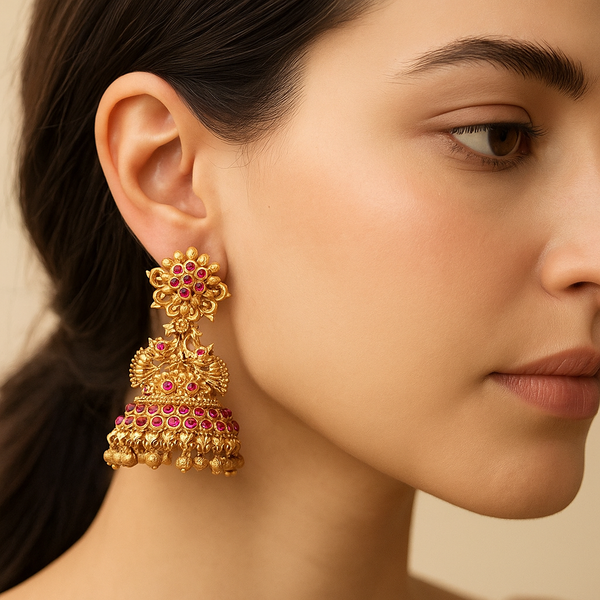 Close-up of a woman wearing a gold and ruby gemstone jhumka earring.