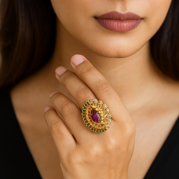 Close-up of a woman's hand wearing a gold ring with a purple gemstone, against a blurred background.