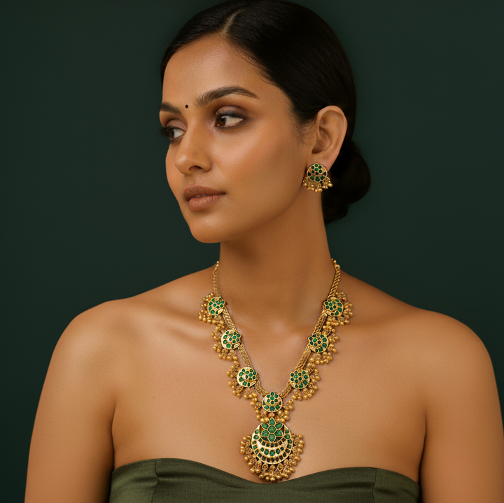 Woman wearing a green and gold necklace and earrings with golden pearls.